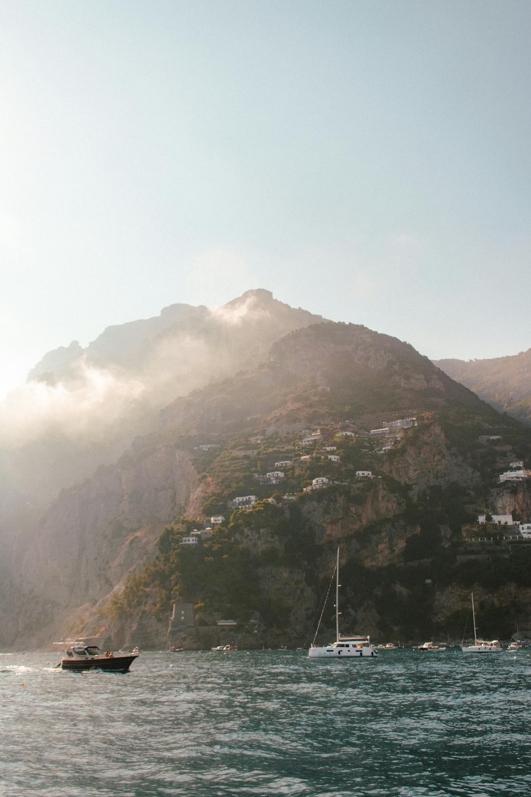 A breathtaking view of Positano's coastal cliffs and boats under a misty sky, capturing Italy's allure.