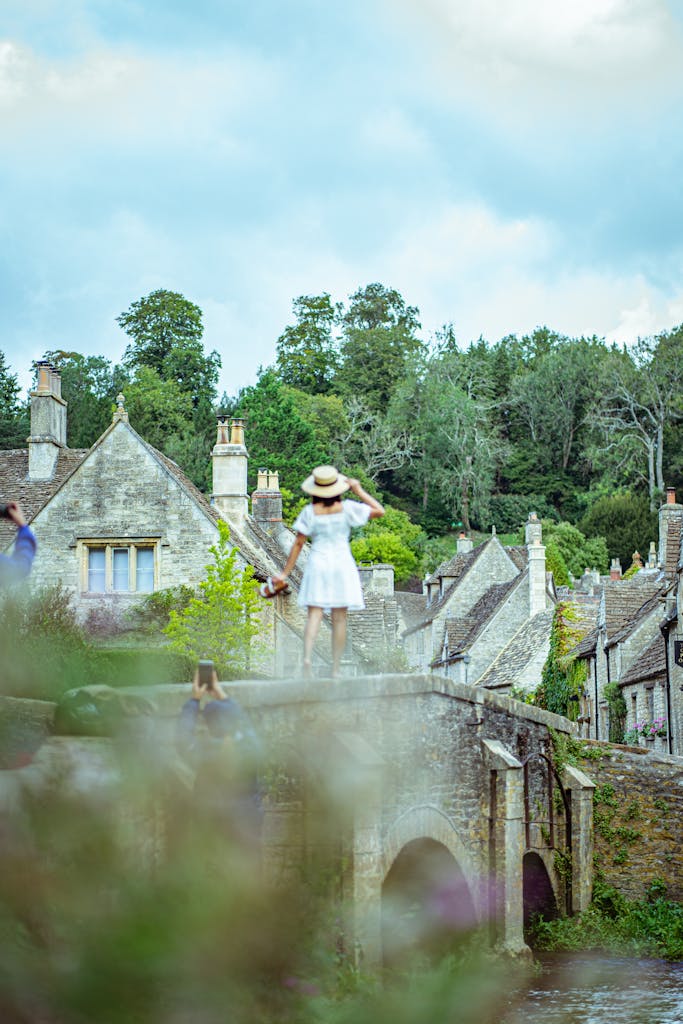 A scenic view of Castle Combe, UK featuring a woman in a dress enjoying a summer day.
