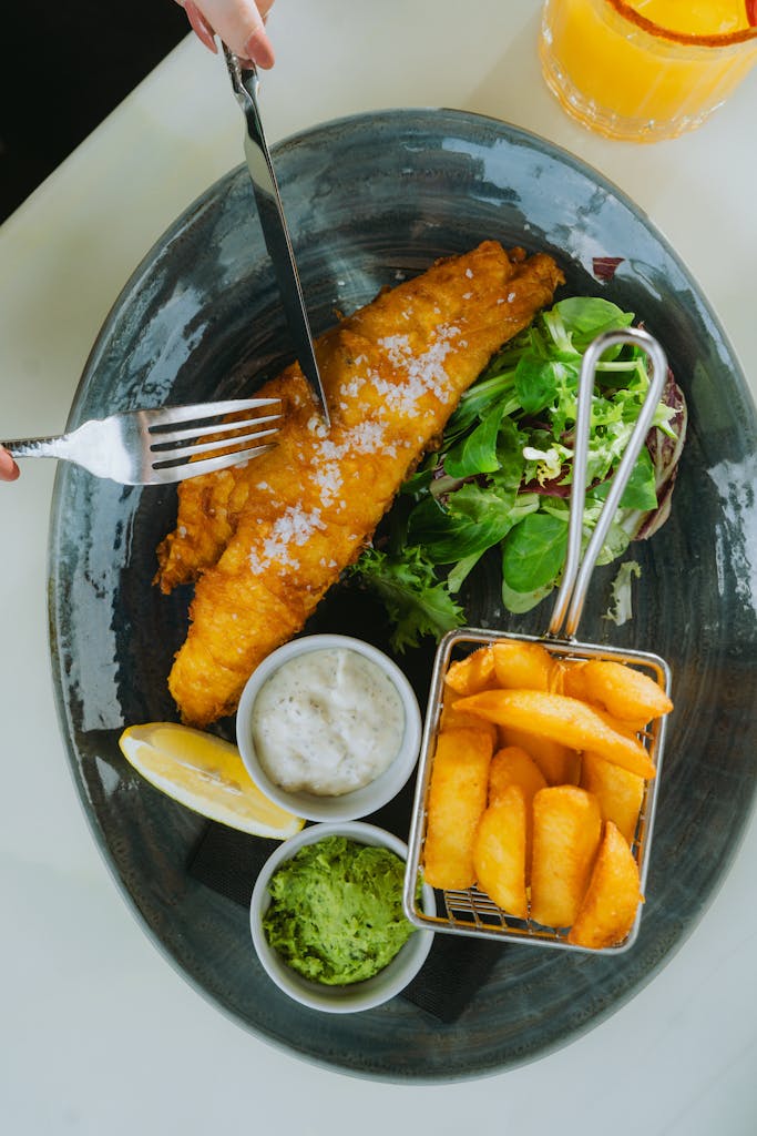 A vibrant plate of fish and chips with salad and sauces, captured in a top view.