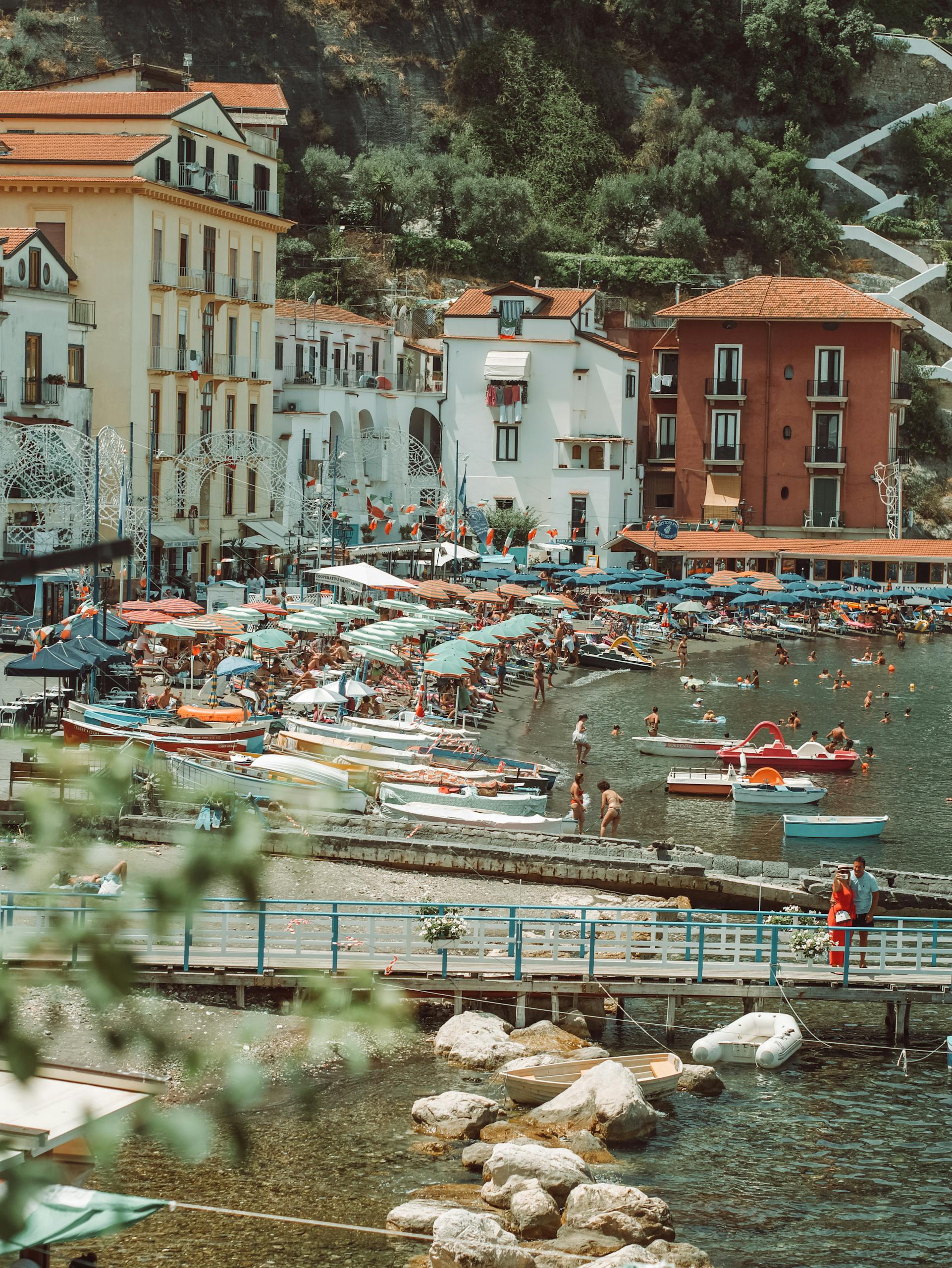 A vibrant summer beach scene in Sorrento, Italy with colorful umbrellas and boats along the shoreline.