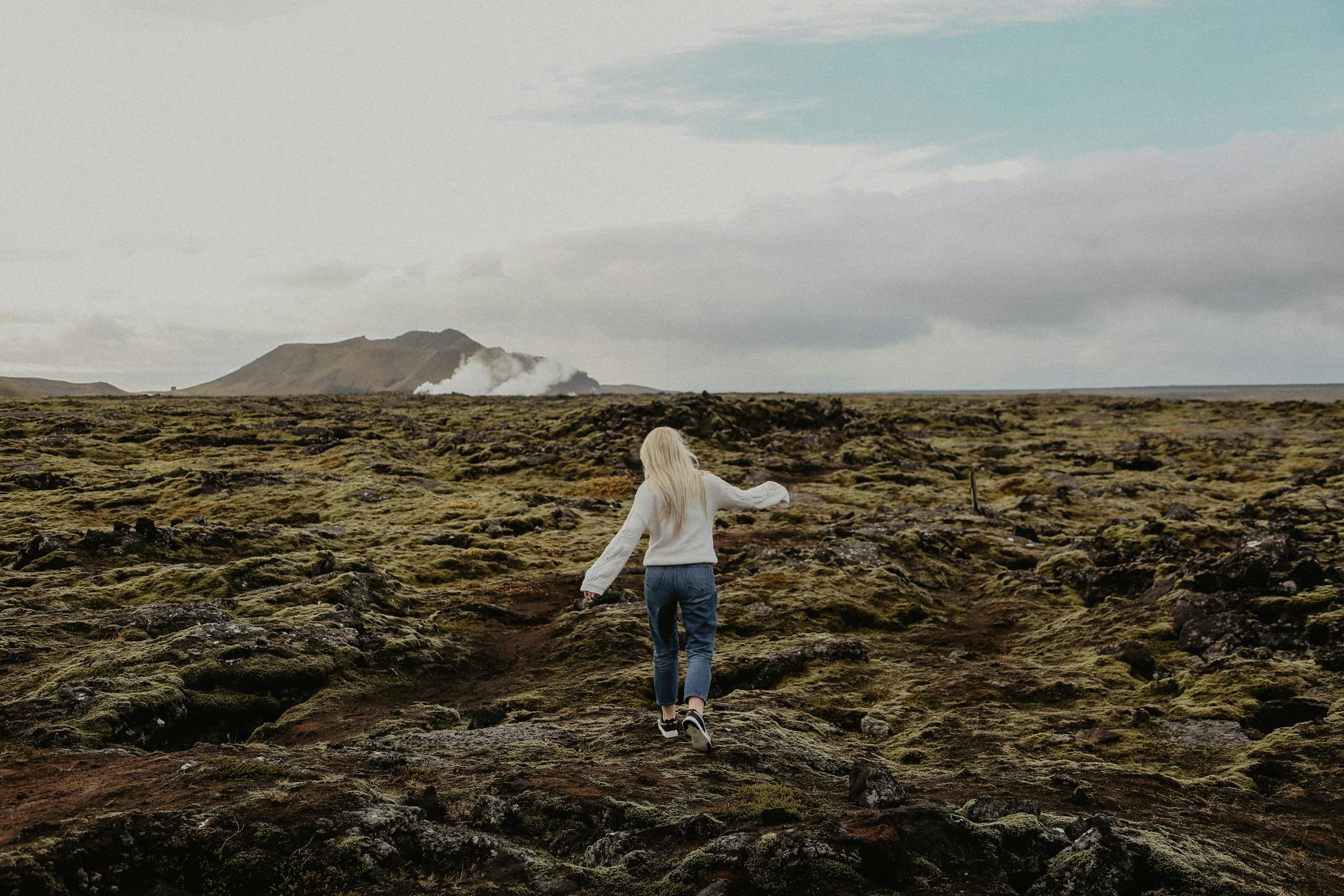 A woman walks across a rocky terrain in Iceland, embracing nature and adventure.