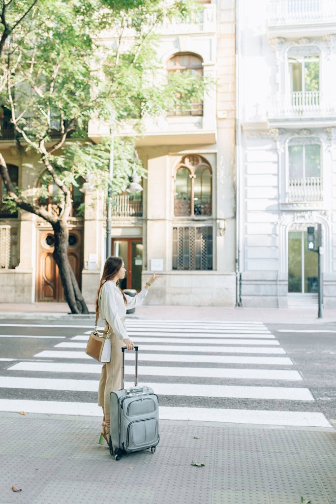 A young woman with a suitcase stands at a city crosswalk, pointing forward.