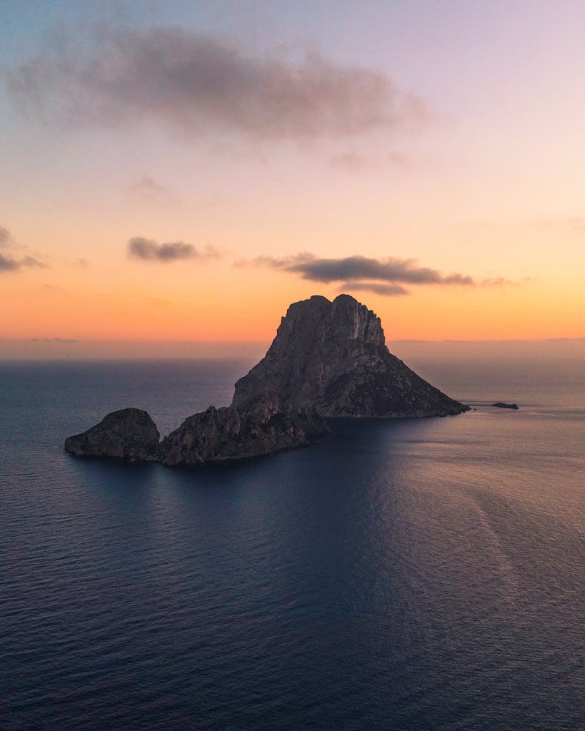 Aerial view of the iconic Es VedrĂ island in Ibiza, captured at sunset with vibrant skies and calm sea.