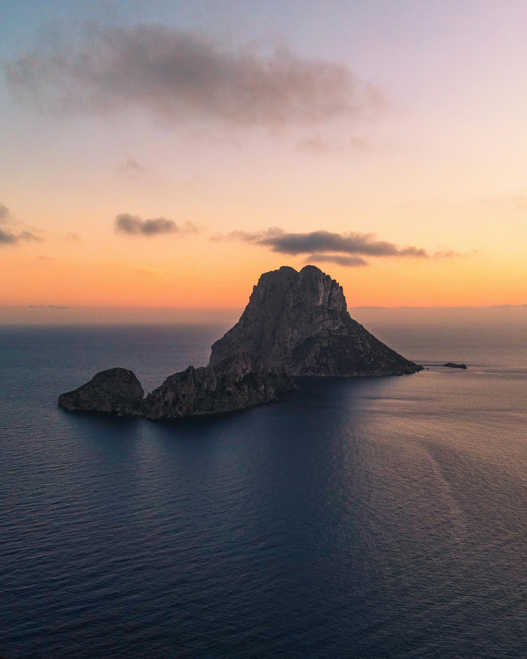 Aerial view of the iconic Es Vedrà island in Ibiza, captured at sunset with vibrant skies and calm sea.