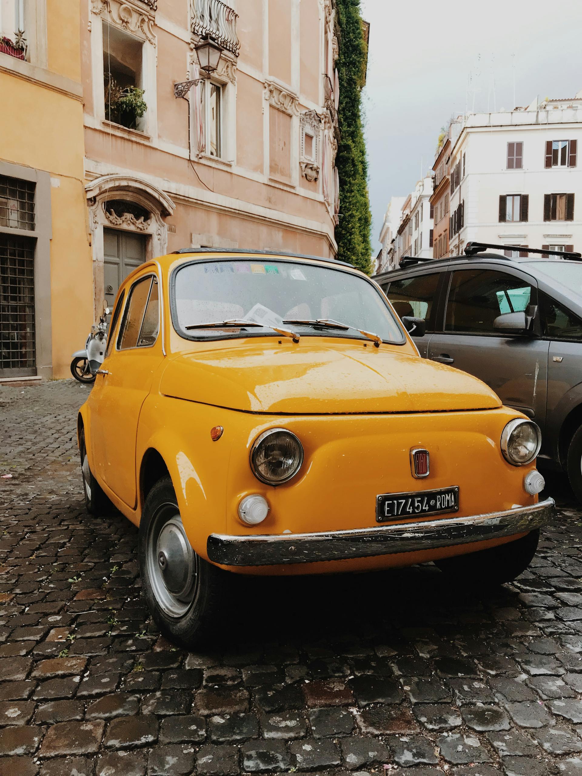 Classic yellow Fiat 500 on a cobblestone street in Rome, Italy, embodying vintage Italian style.