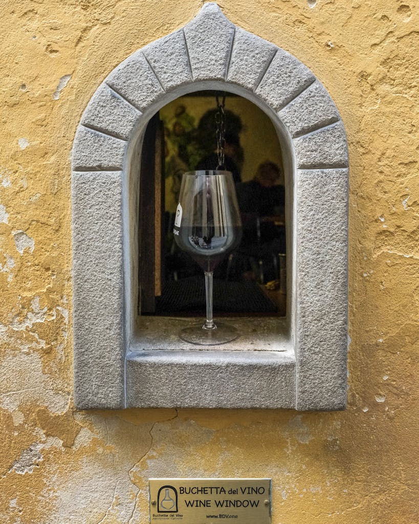 Close-up of a wine window with a glass of red wine in Florence, Italy, showcasing Italian tradition.