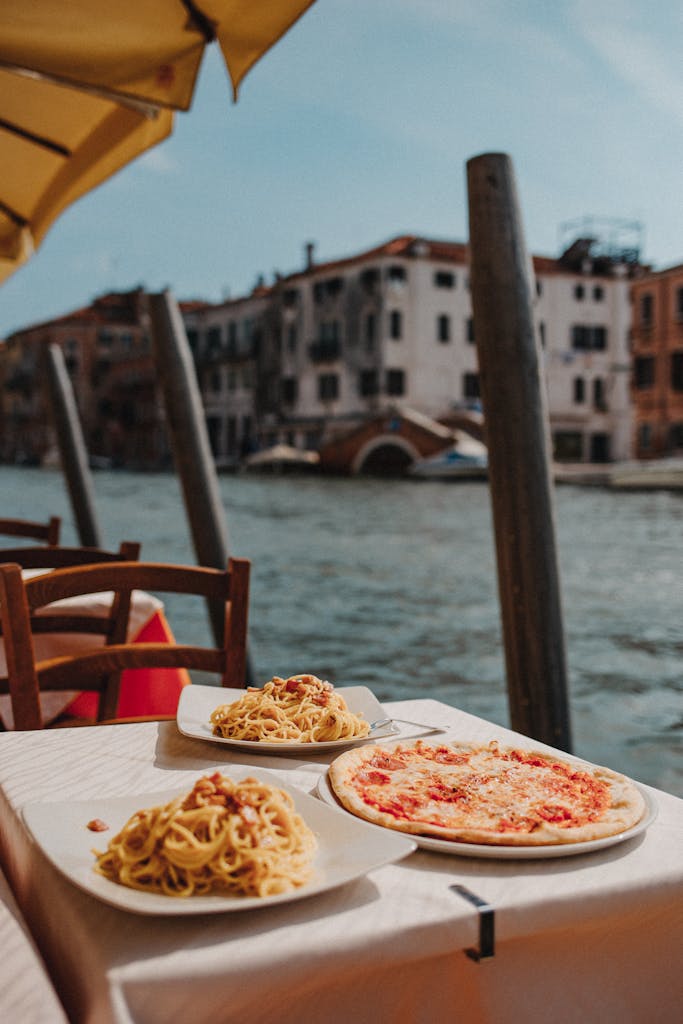 Delightful Italian pasta and pizza served by the scenic Venetian canal under sunny skies.
