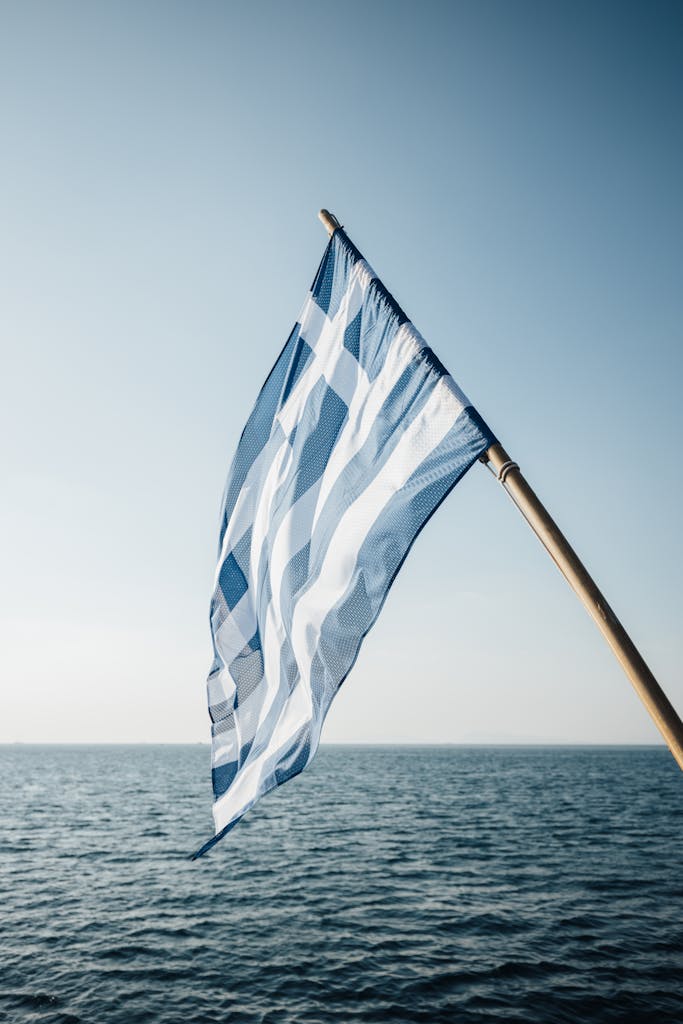 Greek flag waving over the Aegean Sea under a clear sky, symbolizing national pride and maritime tradition.