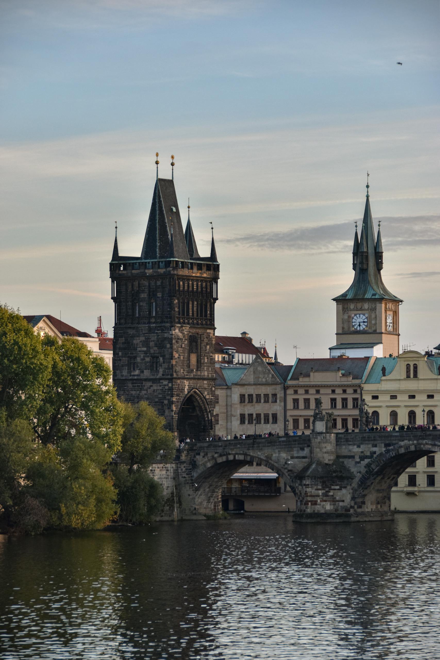 Iconic view of Charles Bridge in Prague, featuring historic towers and tranquil river scene at sunset.