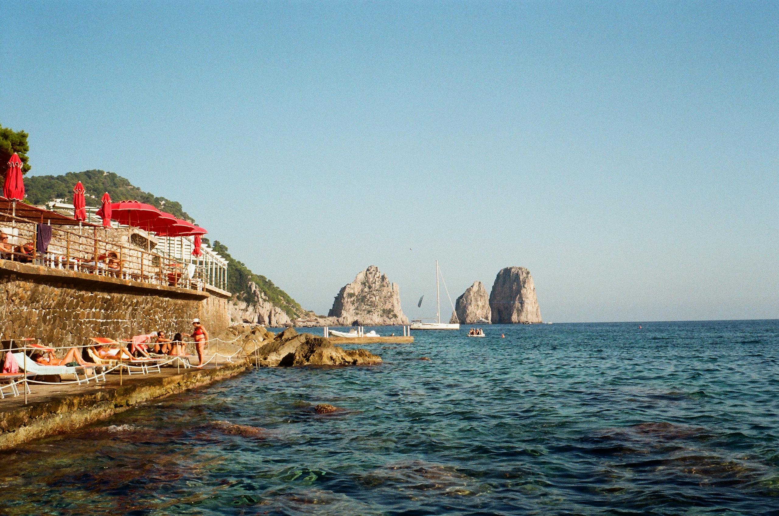 Relaxing seaside view with sunbathers in Capri, Italy, featuring clear blue skies and tranquil waters.