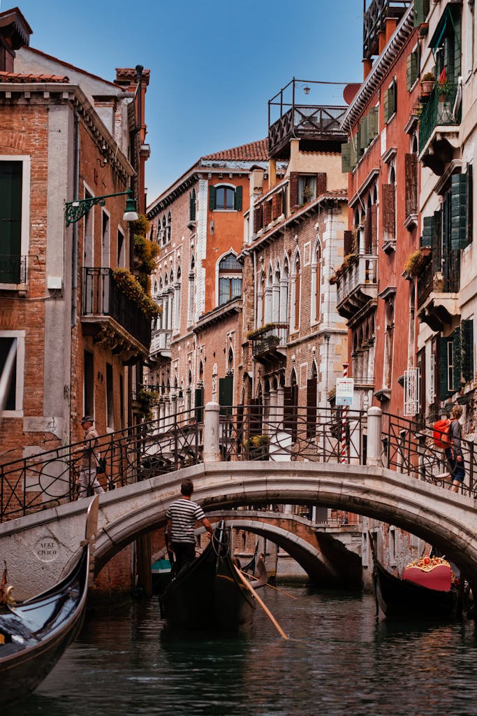Sunlit canal in Venice with gondolas and historic architecture under a blue sky.