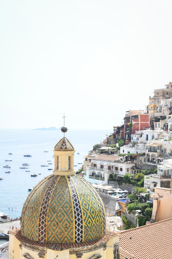 The beautiful dome of Santa Maria Assunta church against Positano's colorful cliffside and blue sea.