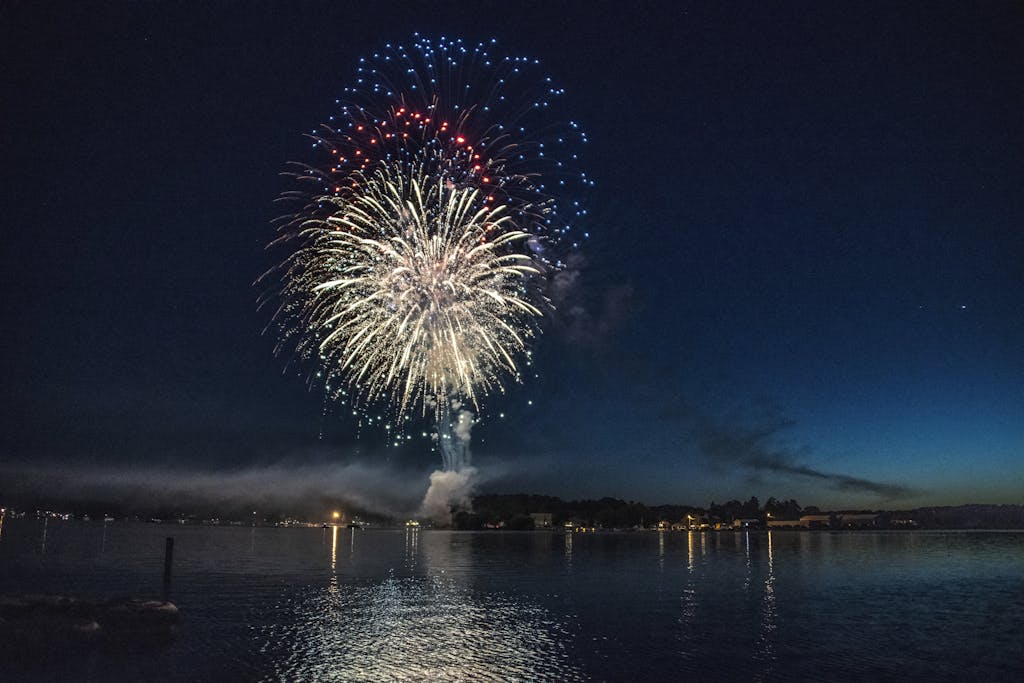 Vibrant fireworks illuminate the night sky over a serene lake, reflecting colors in East Berlin, PA.