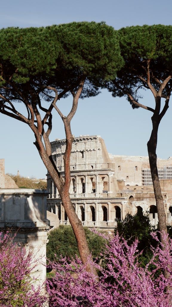 Vibrant spring view of the Colosseum in Rome framed by lush trees and flowers.