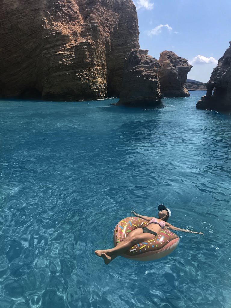 Woman floats on inflatable in clear blue water near Paros' rocky coastline, Greece.