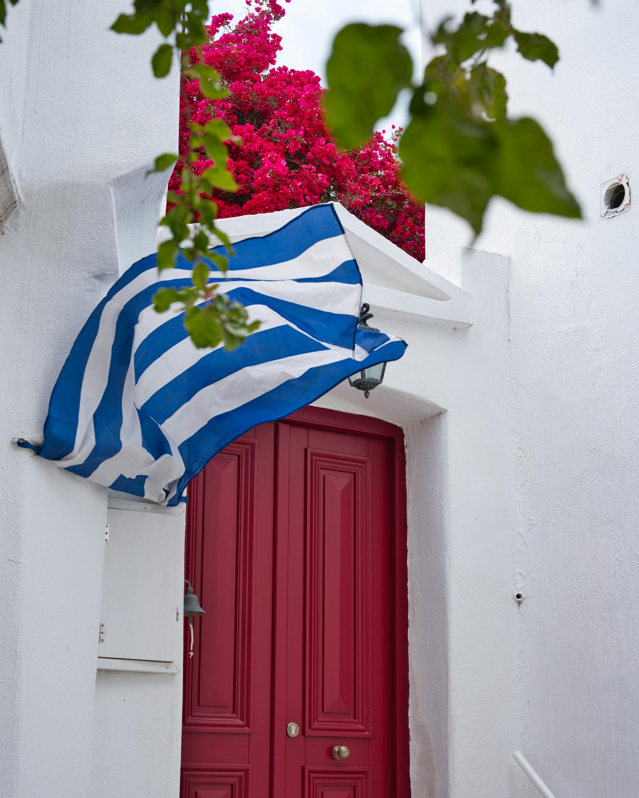 A picturesque red door in Lefkes, Greece, with a Greek flag and bougainvillea.