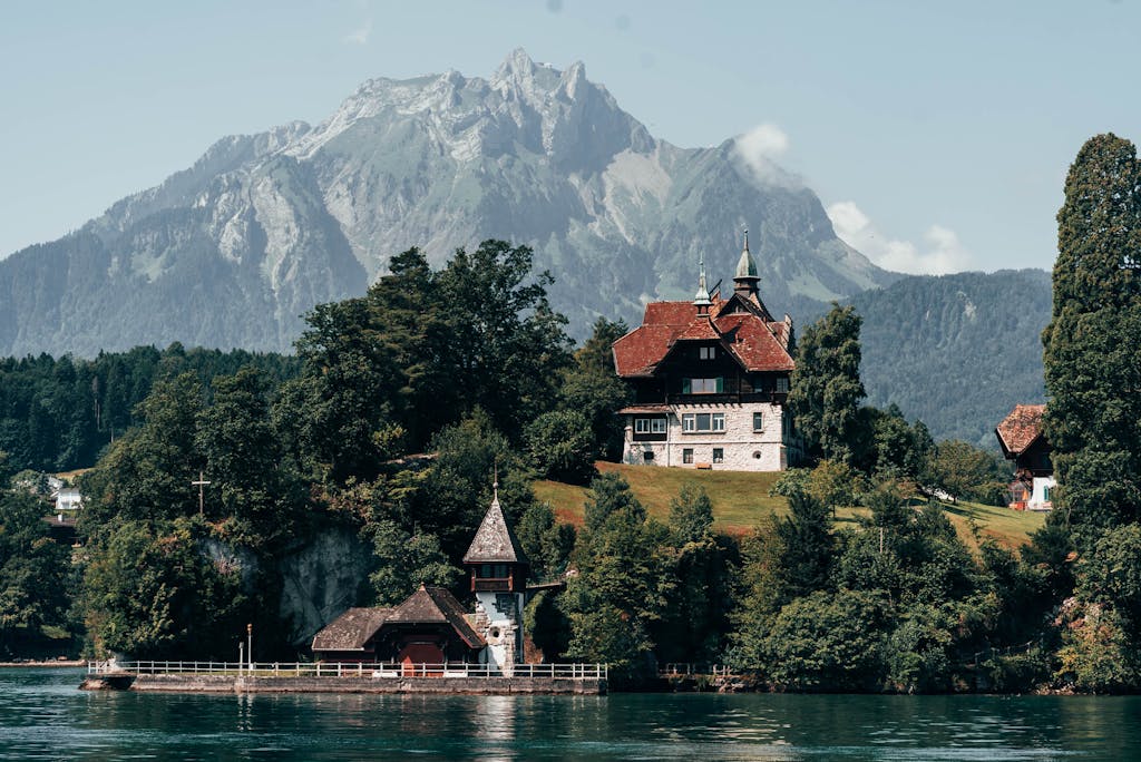 Charming villa by a lake in Lucerne, Switzerland, surrounded by mountains and trees.