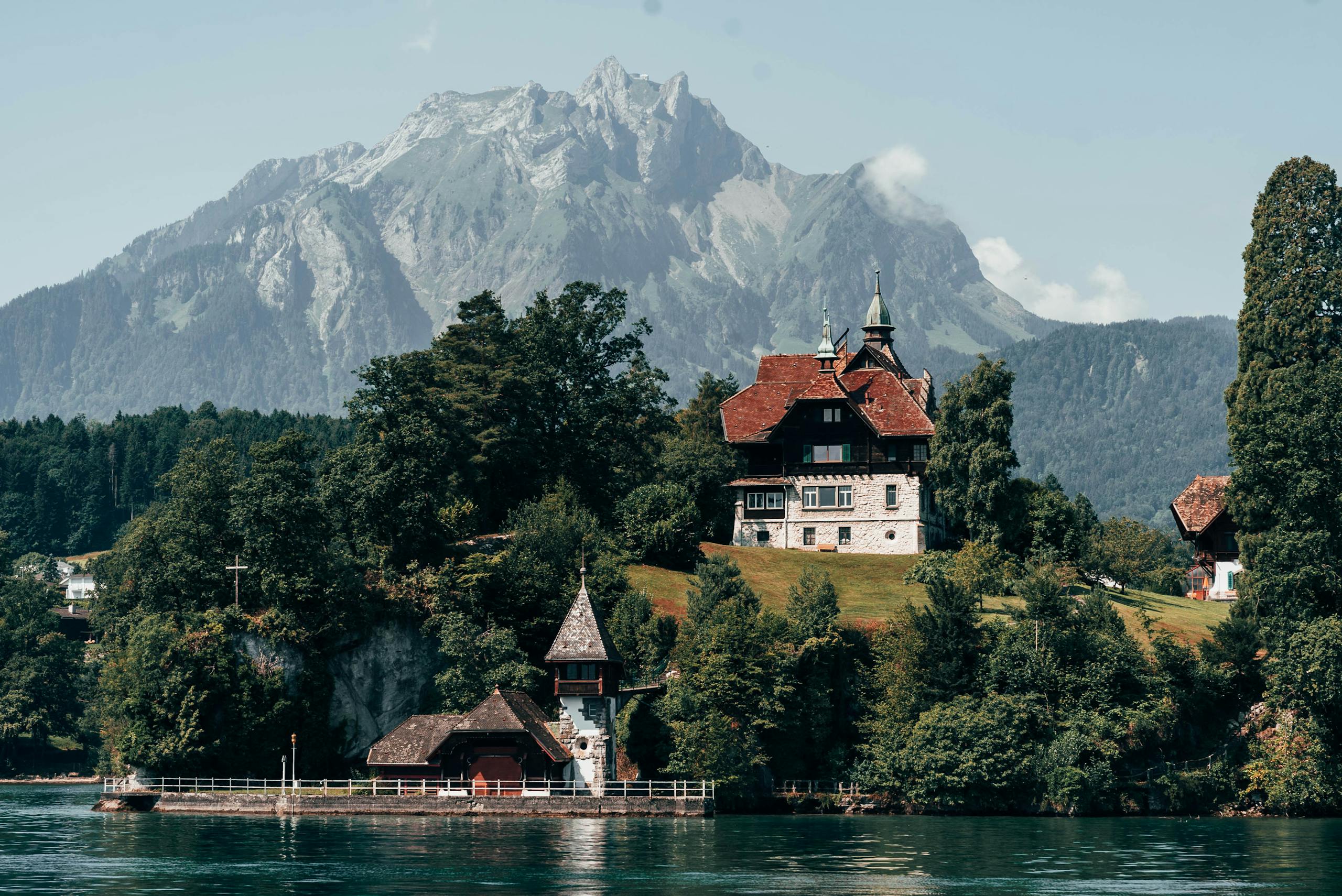 Charming villa by a lake in Lucerne, Switzerland, surrounded by mountains and trees.