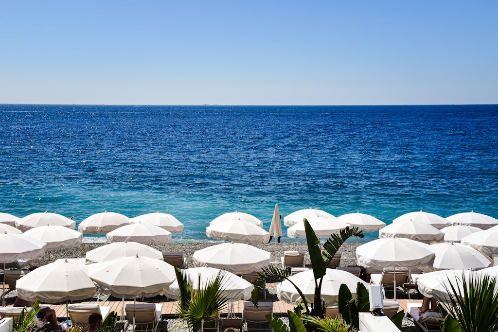 Sunny day at a picturesque beach in Provence-Alpes-Côte d'Azur, France, with white umbrellas and blue sea.