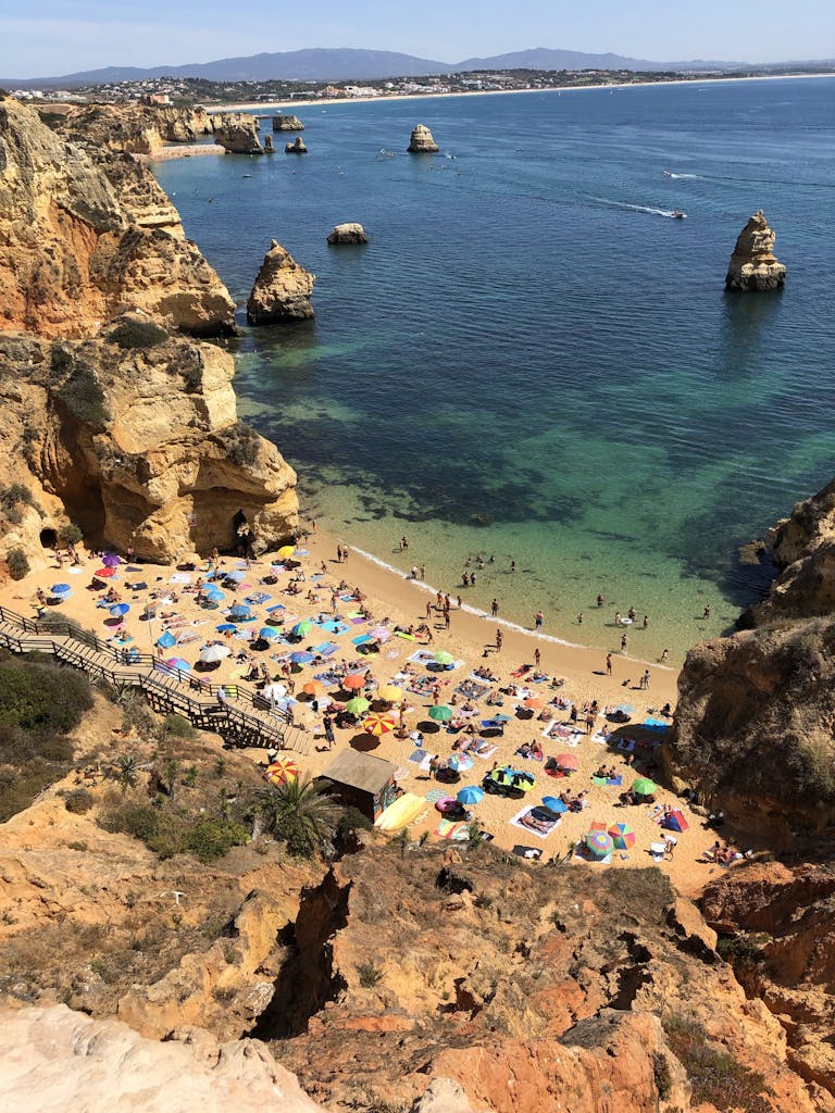 A breathtaking aerial shot of Algarve beach with sunbathers, rocks, and vibrant umbrellas.