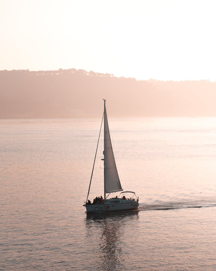 A serene view of a sailboat gliding on the Tagus River during a Lisbon sunset.