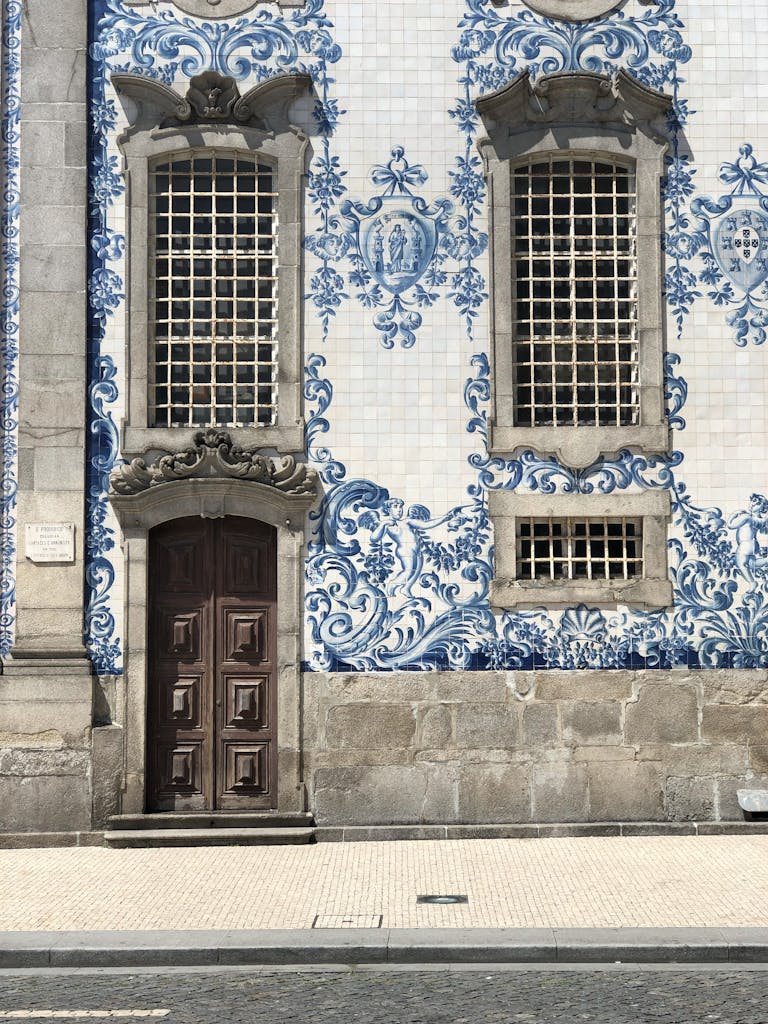 Intricate blue and white tiled facade with ornate windows and a wooden door in Porto, Portugal.