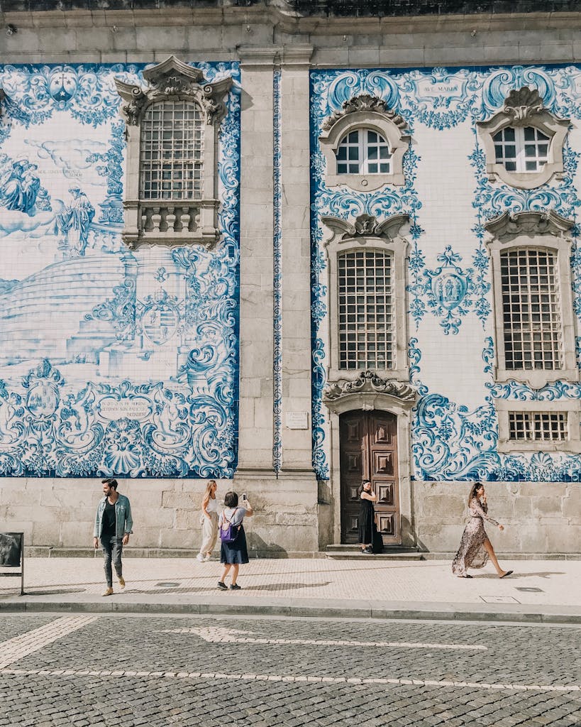 Ornate blue azulejo tiles adorn a historic building in Porto, Portugal, with people walking by.