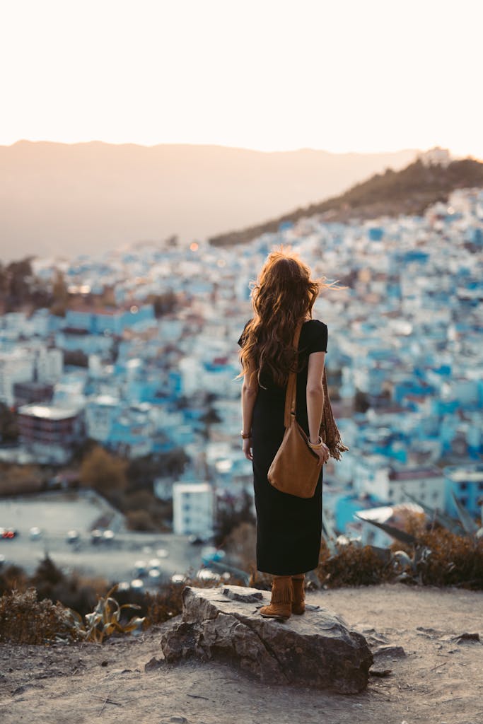 A woman stands on a rock, admiring the panoramic view of Chefchaouen, Morocco at sunset.